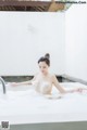 A woman sitting in a bathtub with foam on her body.