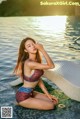 A woman in a bikini sitting on the edge of a swimming pool.