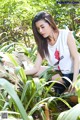 A woman crouching down in the middle of a lush green forest.