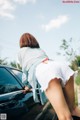 A woman leaning on the hood of a black car.