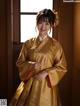 A woman in a yellow hanbok standing in front of a window.