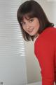 A woman in a red shirt leaning against a wall.