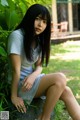 A woman sitting on a rock in the grass.