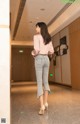 A woman in a pink blouse and jeans standing in a hallway.