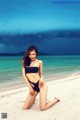 A woman in a black bikini sitting on a beach.