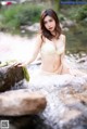 A woman in a white bikini sitting on a rock in a river.