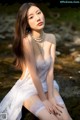 A woman in a white dress sitting on a rock by the water.