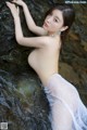 A woman in a white dress leaning against a rock in the water.